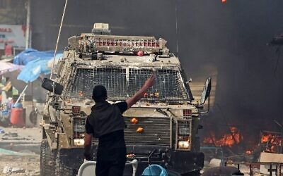Un Palestinien faisant face à un véhicule militaire israélien lors d'une opération dans la ville de Naplouse en Cisjordanie, le 22 février 2023. (Crédit : Zain Jaafar/AFP)
