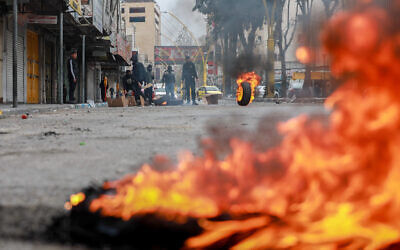 Des Palestiniens brûlent des pneus lors d'affrontements avec les forces israéliennes dans la ville d'Hébron en Cisjordanie, le 23 février 2023. (Crédit : Wisam Hashlamoun/Flash90)