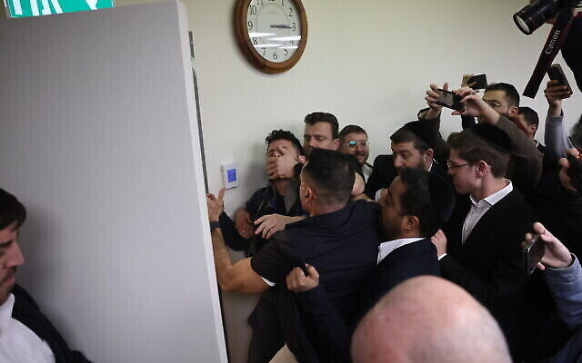 Des gardes de sécurité attrapent et expulsent un manifestant anti-gouvernemental qui a interrompu le discours du chef du parti Shas Aryeh Deri lors d'une réunion de faction à la Knesset à Jérusalem, le 13 février 2023. (Crédit : Yonatan Sindel/Flash90)