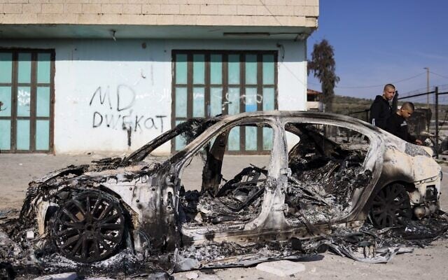 Des Palestiniens passant devant une voiture incendiée dans la ville de Huwara, en Cisjordanie, le 27 février 2023. (Crédit : Ronaldo Schemidt/AFP)