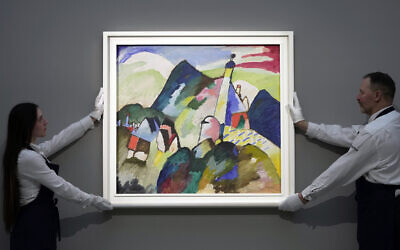 Des membres du personnel tiennent le tableau "Murnau avec l'église II" de l'artiste russe Wassily Kandinsky en 1910, exposé lors d'une avant-première médiatique de la vente aux enchères de Sotheby's, à Londres, le 22 février 2023. (Crédit : AP Photo/Kin Cheung)