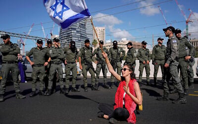 Une manifestante brandissant le drapeau israélien, assise sur une autoroute et encadrée par la police des frontières, lors d'une manifestation contre les projets du gouvernement du Premier ministre Benjamin Netanyahu de remanier le système judiciaire, à Tel Aviv, Israël, le 9 mars 2023. (Crédit : AP Photo/Ariel Schalit)