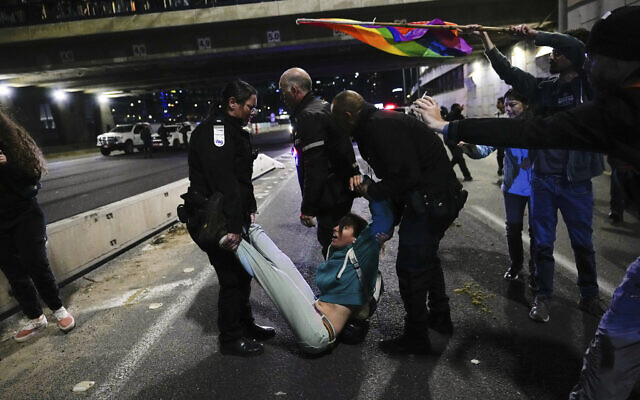 Des policiers israéliens évacuant des manifestants qui bloquent une autoroute lors d'une protestation contre les projets du gouvernement du Premier ministre Benjamin Netanyahu de réformer le système judiciaire israélien, à Tel Aviv, Israël, le 18 mars 2023. (Crédit : Ohad Zwigenberg/AP) Des policiers israéliens évacuant des manifestants qui bloquent une autoroute lors d'une protestation contre les projets du gouvernement du Premier ministre Benjamin Netanyahu de réformer le système judiciaire israélien, à Tel Aviv, Israël, le 18 mars 2023. (Crédit : Ohad Zwigenberg/AP)