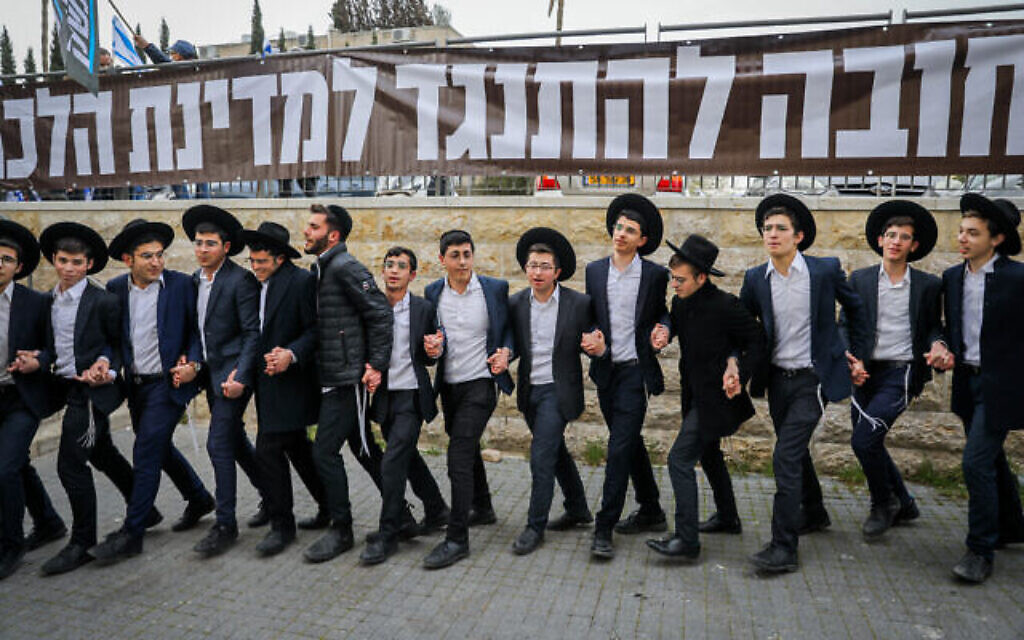 De jeunes hommes juifs ultra-orthodoxes dansent alors qu'une manifestation contre la refonte judiciaire se déroule devant le domicile du chef du parti Shas Aryeh Deri à Jérusalem, le 23 mars 2023. (Crédit : Flash90)