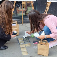 Des bénévoles juifs nettoyant des Stolpersteine (pierres d'achoppement) à Bruxelles, en Belgique, lors d'un événement de nettoyage des Stolpersteine organisé conjointement avec l'Association juive européenne à l'occasion de Yom HaShoah, le 27 avril 2022. (Crédit : Make Their Memory Shine)
