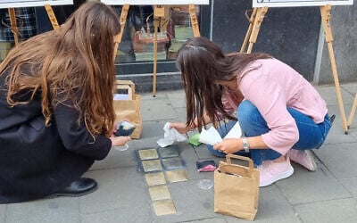 Des bénévoles juifs nettoyant des Stolpersteine (pierres d'achoppement) à Bruxelles, en Belgique, lors d'un événement de nettoyage des Stolpersteine organisé conjointement avec l'Association juive européenne à l'occasion de Yom HaShoah, le 27 avril 2022. (Crédit : Make Their Memory Shine)