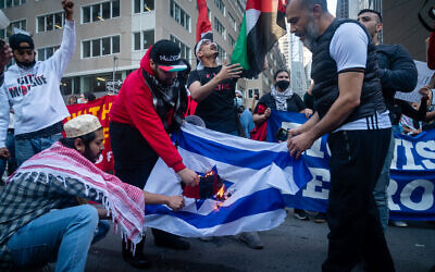Des manifestants pro-palestiniens et anti-Israël brûlant un drapeau israélien, à New York, le 15 mai 2021. (Crédit : Luke Tress/Times of Israel)