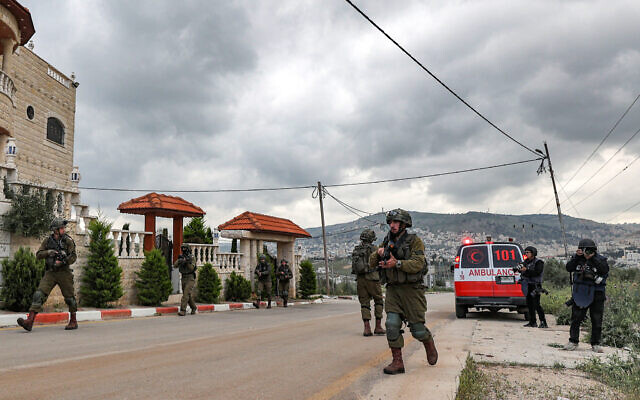 Des journalistes, à droite, se tenant près d'une ambulance alors que des soldats israéliens marchent pendant une opération de l'armée près de l'implantation d'Elon Moreh, en Cisjordanie près de Naplouse, le 11 avril 2023. (Crédit : Jaafar Ashtiyeh/AFP) Des journalistes, à droite, se tenant près d'une ambulance alors que des soldats israéliens marchent pendant une opération de l'armée près de l'implantation d'Elon Moreh, en Cisjordanie près de Naplouse, le 11 avril 2023. (Crédit : Jaafar Ashtiyeh/AFP)