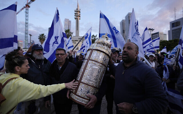 Des Israéliens de droite marchant avec la Torah lors d'un rassemblement de soutien aux plans du gouvernement du Premier ministre Benjamin Netanyahu visant à réformer le système judiciaire, à Tel Aviv, le 30 mars 2023. (Crédit : Ariel Schalit/AP) Des Israéliens de droite marchant avec la Torah lors d'un rassemblement de soutien aux plans du gouvernement du Premier ministre Benjamin Netanyahu visant à réformer le système judiciaire, à Tel Aviv, le 30 mars 2023. (Crédit : Ariel Schalit/AP)