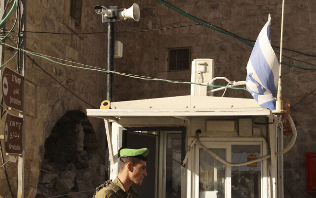 Un soldat israélien se tient sous une caméra de surveillance à un point de contrôle dans la ville palestinienne d'Hébron le 9 novembre 2021 (Crédit : HAZEM BADER/AFP) Un soldat israélien se tient sous une caméra de surveillance à un point de contrôle dans la ville palestinienne d'Hébron le 9 novembre 2021 (Crédit : HAZEM BADER/AFP)