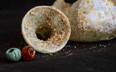 Un récipient en verre et des perles de verre découverts dans une grotte funéraire vieille de 1 800 ans, dans le nord d'Israël, qui a failli être détruite par des travaux de construction, en mai 2023. (Crédit : Autorisation/Yoli Schwartz/IAA)
