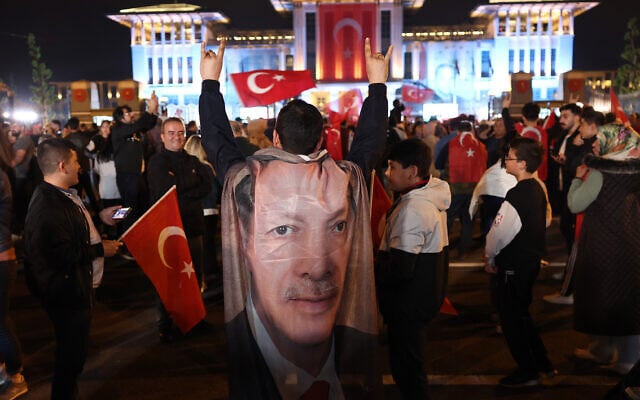 Un partisan du président turc Recep Tayyip Erdogan porte un drapeau à son effigie sur ses épaules et fait le Bozkurt isareti (salut du loup gris), un symbole nationaliste turc et pan-turc de la main, alors que les gens célèbrent sa victoire au second tour de l'élection présidentielle, devant le palais présidentiel d'Ankara, le 29 mai 2023. (Crédit: Adem ALTAN / AFP) Un partisan du président turc Recep Tayyip Erdogan porte un drapeau à son effigie sur ses épaules et fait le Bozkurt isareti (salut du loup gris), un symbole nationaliste turc et pan-turc de la main, alors que les gens célèbrent sa victoire au second tour de l'élection présidentielle, devant le palais présidentiel d'Ankara, le 29 mai 2023. (Crédit: Adem ALTAN / AFP)