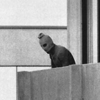 Un élément du groupe terroriste qui a enlevé les membres de l'équipe olympique israélienne dans leurs quartiers au village olympique apparaissant avec une cagoule sur son visage se tient sur le balcon du bâtiment où ils ont tenu les membres de l'équipe israélienne en otage à Munich, le 5 septembre 1972. (Crédit : Kurt Strumpf/AP)