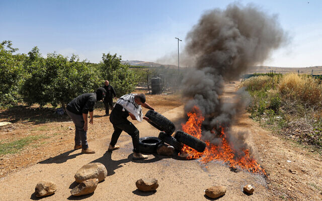 Des membres de la communauté druze mettent le feu à des pneus alors qu'ils protestent contre un projet israélien d'éoliennes prévu sur des terres agricoles près du village de Majdal Shams, sur les hauteurs du Golan, le 21 juin 2023. (Crédit : Jalaa MAREY / AFP)