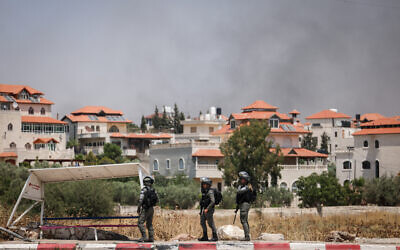 De la fumée s'élève derrière les soldats de Tsahal à l'entrée de Turmus Ayya, alors que des dizaines d'habitants des implantations se seraient déchaînés dans le village de Cisjordanie, le 21 juin 2023 (Crédit : Yonatan Sindel/Flash90)