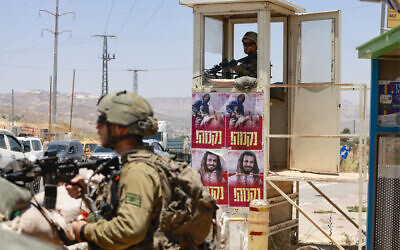 Des affiches portant les portraits d'Israéliens récemment tués par des terroristes palestiniens, avec "vengeance" écrit en dessous en hébreu, sont placardées le long de la gare routière de Tapuach en Cisjordanie, gardée par des soldats israéliens, le 25 juin 2023. (Crédit : Menahem Kahana/AFP)
