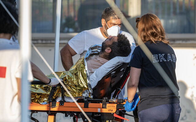 Des membres du personnel médical transportent un survivant sur une civière à l'extérieur d'un entrepôt dans le port de la ville de Kalamata, le 14 juin 2023, après le naufrage d'un bateau transportant des dizaines de migrants dans les eaux internationales de la mer Ionienne. (Crédit : Angelos Tzortzinis / AFP)