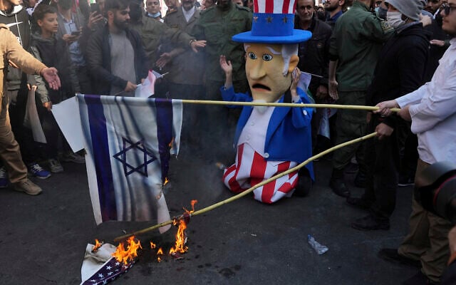 Des manifestants brûlant des représentations des drapeaux américain et israélien tandis qu'un personnage de l'Oncle Sam "réagit" lors d'une manifestation annuelle devant l'ancienne ambassade des États-Unis à Téhéran, en Iran, le 4 novembre 2022. (Crédit : AP Photo/Vahid Salemi)