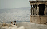Illustration : Des touristes marchent devant les statues des cariatides qui soutiennent le porche du temple de l'Erechthéion, datant du Ve siècle avant J.-C., sur la colline de l'Acropole, alors que l'on voit la ville d'Athènes en arrière-plan, le 20 septembre 2011. (Crédit : Petros Giannakouris/AP)