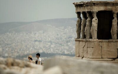 Illustration : Des touristes marchent devant les statues des cariatides qui soutiennent le porche du temple de l'Erechthéion, datant du Ve siècle avant J.-C., sur la colline de l'Acropole, alors que l'on voit la ville d'Athènes en arrière-plan, le 20 septembre 2011. (Crédit : Petros Giannakouris/AP)