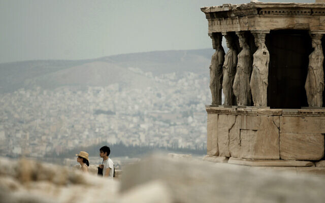 Illustration : Des touristes marchent devant les statues des cariatides qui soutiennent le porche du temple de l'Erechthéion, datant du Ve siècle avant J.-C., sur la colline de l'Acropole, alors que l'on voit la ville d'Athènes en arrière-plan, le 20 septembre 2011. (Crédit : Petros Giannakouris/AP)