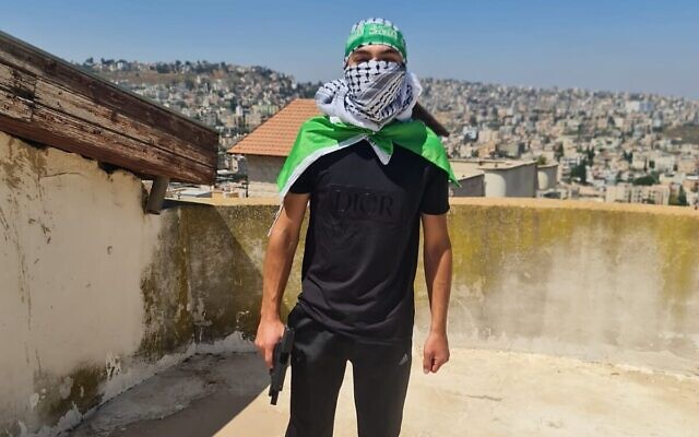 Un suspect détenu par la police pour son affiliation présumée au Hamas est vu, dans une image publiée par la police, brandissant une arme de poing sur le toit de sa maison dans la région de Nazareth, dans le nord d'Israël, le 10 juillet 2023. (Crédit : Police israélienne) Un suspect détenu par la police pour son affiliation présumée au Hamas est vu, dans une image publiée par la police, brandissant une arme de poing sur le toit de sa maison dans la région de Nazareth, dans le nord d'Israël, le 10 juillet 2023. (Crédit : Police israélienne)