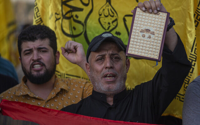 Un Irakien brandit un Coran lors d'une manifestation sur la place Tahrir, à Bagdad, en Irak, le jeudi 20 juillet 2023. (Crédit : Adil AL-Khazali/AP) Un Irakien brandit un Coran lors d'une manifestation sur la place Tahrir, à Bagdad, en Irak, le jeudi 20 juillet 2023. (Crédit : Adil AL-Khazali/AP)
