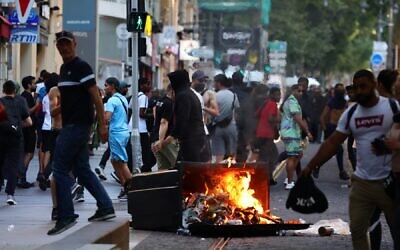 Des manifestants passant devant une poubelle brûlée lors d'affrontements avec la police, après une quatrième nuit consécutive d'émeutes en France à la suite du meurtre d'un adolescent par la police, à Marseille, dans le sud de la France, le 1er juillet 2023. (Crédit : Clement Mahoudeau/AFP)