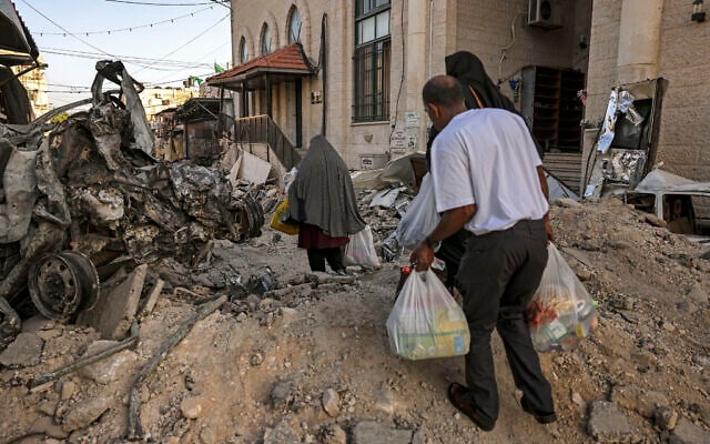 Des gens transportant des sacs contenant des marchandises données par une organisation locale alors qu'ils marchent parmi les débris à la suite d'une opération militaire de Tsahal dans le camp de réfugiés de Jénine, en Cisjordanie, le 5 juillet 2023. (Crédit : Ronaldo Schemidt/AFP)