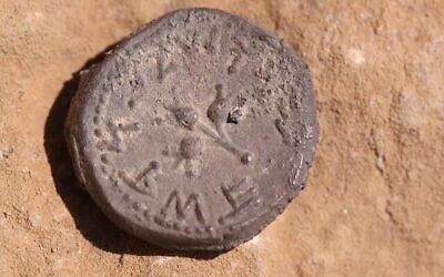 La pièce vieille de 2 000 ans telle qu'elle a été découverte dans une grotte près d'Ein Gedi, avec trois grenades et les mots "Sainte Jérusalem" en écriture ancienne. (Crédit : Emil Aladjem/IAA)