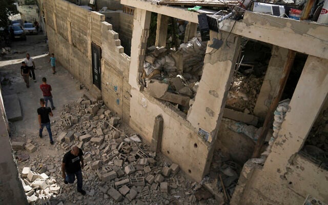Des Palestiniens passant devant une maison endommagée, après que l'armée israélienne a retiré ses forces du bastion terroriste, dans le camp de réfugiés de Jénine en Cisjordanie, le 5 juillet 2023. (Crédit : AP Photo/Nasser Nasser)
