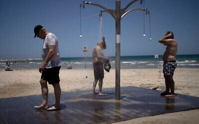 Photo d'illustration : Des hommes se douchent sur une plage publique pour se rafraichir des fortes chaleurs à Tel Aviv, en Israël, le jeudi 13 juillet 2023. Le service météorologique israélien a émis un avertissement de fortes chaleurs et mis en garde contre le risque de déshydratation et de coups de chaleur. (Crédit : AP/Maya Alleruzzo)