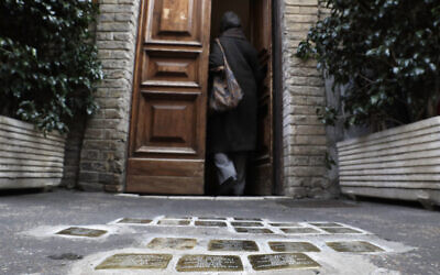 Illustration : Une femme entrant dans un bâtiment où des pierres d'achoppement, gravées de noms de Juifs tués par les nazis, sont visibles devant l'entrée, dans le quartier juif du Ghetto de Rome, le 27 janvier 2021. (Crédit : Gregorio Borgia/AP)