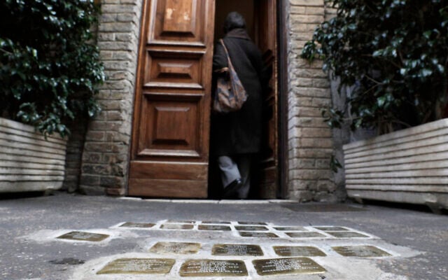 Illustration : Une femme entrant dans un bâtiment où des pierres d'achoppement, gravées de noms de Juifs tués par les nazis, sont visibles devant l'entrée, dans le quartier juif du Ghetto de Rome, le 27 janvier 2021. (Crédit : Gregorio Borgia/AP)