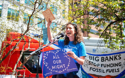 La femme rabbin Laura Bellows, aujourd'hui directrice de l'activisme spirituel et de l'éducation de Dayenu, agite de la matzah alors qu'elle encourage les grandes organisations financières à céder des combustibles fossiles lors d'un rassemblement à Washington, DC, le 20 avril 2022. (Crédit : Bora Chung | Survival Media Agency / Dayenu via JTA)