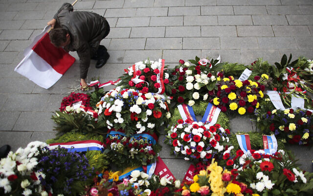 Un homme portant un drapeau polonais déposant des fleurs après une cérémonie de dépôt de gerbes pour commémorer l'invasion de la Pologne par l'Allemagne nazie et le début de la Seconde Guerre mondiale, il y a 75 ans, au mémorial des soldats polonais à Berlin, le 1er septembre 2014. (Crédit : Markus Schreiber/AP)