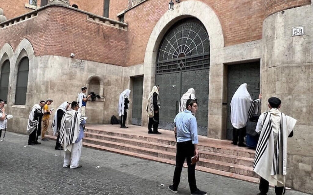 Des fidèles lors de la prière du matin devant les portes verrouillées de la synagogue de la rue Kazinczy à Budapest, en Hongrie, le 21 juillet 2023. (Crédit : David Kelsey/JTA) Des fidèles lors de la prière du matin devant les portes verrouillées de la synagogue de la rue Kazinczy à Budapest, en Hongrie, le 21 juillet 2023. (Crédit : David Kelsey/JTA)