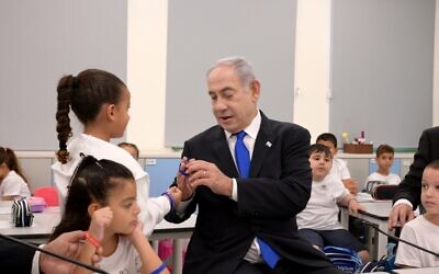 Le Premier ministre Benjamin Netanyahu regarde un bracelet en silicone alors qu'il rend visite à des élèves de première année à Maale Adumim, le 1er septembre 2023. (Crédit : Avi Ohayon/GPO)