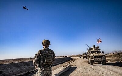 Un hélicoptère d'attaque américain AH-64 Apache survole des soldats américains patrouillant le long des lignes de front entre les zones tenues par les Forces démocratiques syriennes (FDS) et les combattants soutenus par la Turquie, près du village de Dardara dans la campagne de Tal Tamr, dans la province de Hasakeh, au nord-est de la Syrie, le 26 décembre 2021. (Crédit : Delil souleiman/AFP)