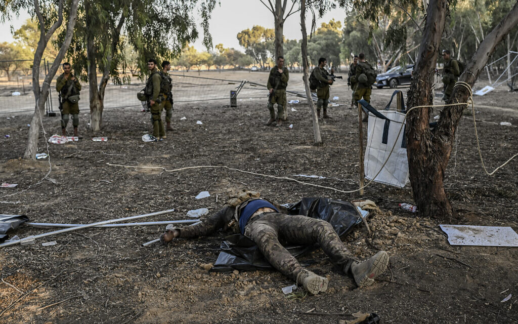 Des soldats israéliens se tiennent derrière le corps d'un terroriste du Hamas mort lors d'une patrouille le 12 octobre 2023 près du kibboutz Beeri, où 270 festivaliers ont été tués par des terroristes lors du festival de musique Supernova le 7 octobre. (Crédit : Aris MESSINIS / AFP)