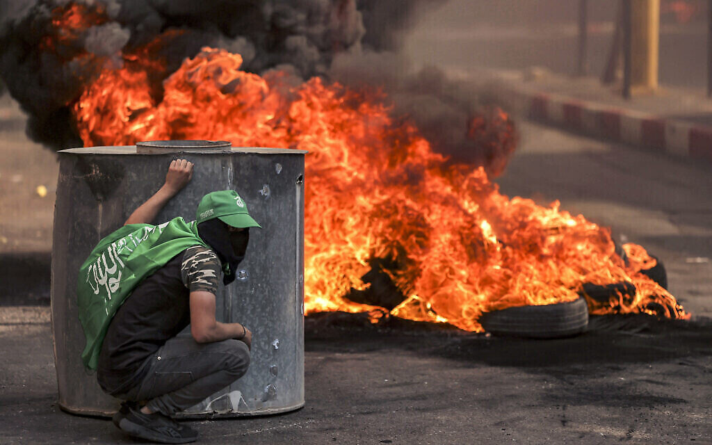 Un manifestant palestinien masqué pendant des affrontements avec les forces israéliennes suite à un rassemblement en solidarité avec Gaza organisé par les partisans du Fatah et du Hamas à Hébron, en Cisjordanie, le 13 octobre 2023. (Crédit :  HAZEM BADER / AFP)