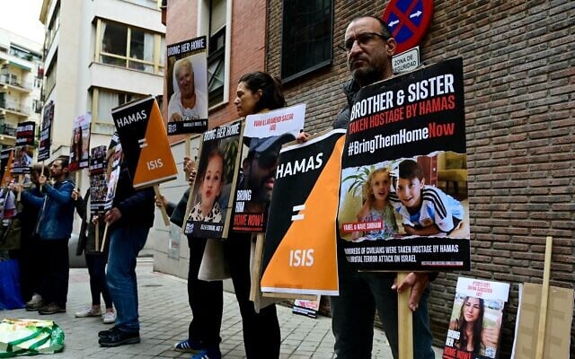 Des parents tiennent des pancartes représentant les Israéliens Margalit Moses, Ella Elyakim, Ivan Illaramendi Saizar, et Yahel et Nave Shoham, retenus en otage par le Hamas après l'attaque du 7 octobre, devant le bâtiment de la Communauté juive de Madrid avant une conférence de presse des familles des citoyens israéliens retenus en otage, à Madrid, le 26 octobre 2023. (Crédit : JAVIER SORIANO / AFP) Des parents tiennent des pancartes représentant les Israéliens Margalit Moses, Ella Elyakim, Ivan Illaramendi Saizar, et Yahel et Nave Shoham, retenus en otage par le Hamas après l'attaque du 7 octobre, devant le bâtiment de la Communauté juive de Madrid avant une conférence de presse des familles des citoyens israéliens retenus en otage, à Madrid, le 26 octobre 2023. (Crédit : JAVIER SORIANO / AFP)