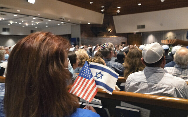 Une femme tenant un drapeau américain et un drapeau israélien lors d'une "veillée pour Israël" à la synagogue Stephen Wise pour prier, chanter et honorer la mémoire des personnes tuées lors du récent massacre en Israël, et pour prier pour la paix et le retour sain et sauf des personnes kidnappées à Los Angeles, le 8 octobre 2023. (Crédit : Richard Vogel/AP Photo) 