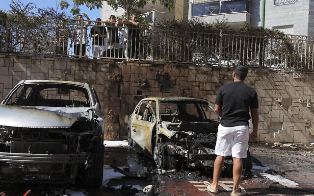Des Israéliens inspectant des voitures endommagées après avoir été touchées par une roquette tirée depuis la bande de Gaza à Ashkelon, dans le sud d'Israël, le 13 octobre 2023. (Crédit : Tsafrir Abayov/AP Photo)