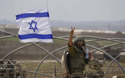 Un soldat israélien fait le signe de la victoire depuis un blindé qui se dirige vers la frontière avec la bande de Gaza, dans le sud d'Israël, le 14 octobre 2023. (Crédit : AP Photo/Ariel Schalit)
