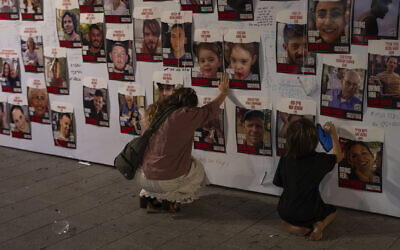Une Israélienne se recueillant en touchant de ses mains les photos d'Israéliens captifs à Gaza, affichées sur un mur, à Tel Aviv, le 21 octobre 2023. (Crédit : Petros Giannakouris/AP)