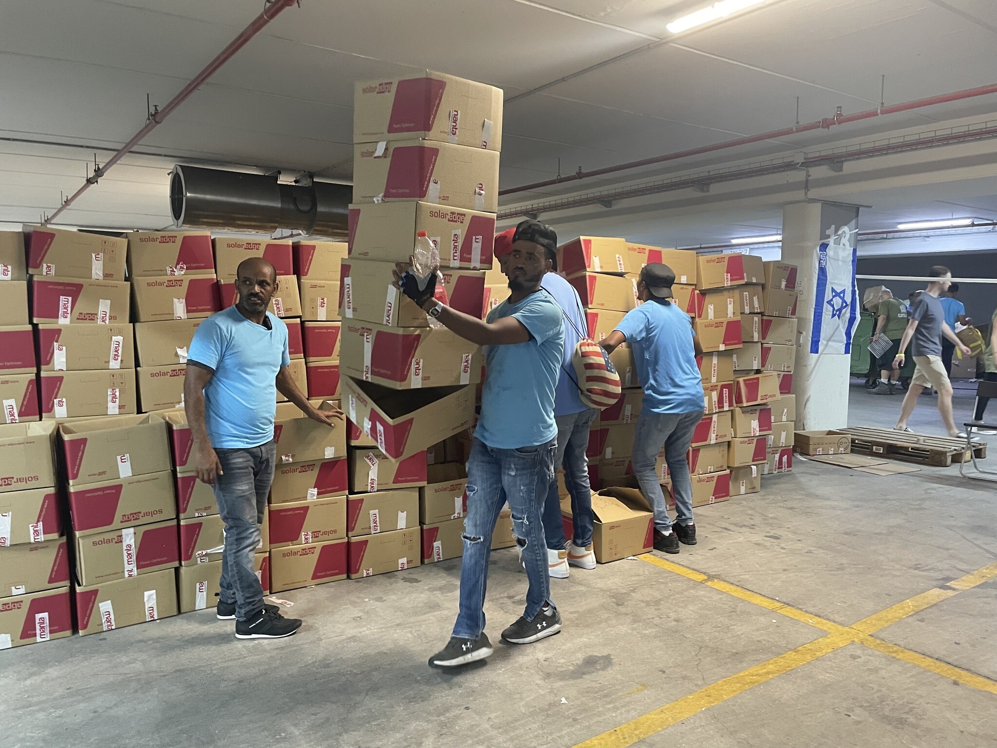 Des demandeurs d'asile érythréens aidant à déplacer des cartons dans une vaste zone de tri souterraine au Centre d'opérations civiles, au centre de convention Expo Tel Aviv, le 19 octobre 2023. (Crédit : Sue Surkes/Times of Israel)