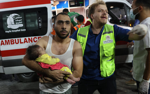 Un homme transporte un bébé palestinien blessé à l'hôpital Al-Shifa dans la ville de Gaza après une frappe aérienne israélienne, le 11 octobre 2023. (Crédit : MOHAMMED ABED / AFP)