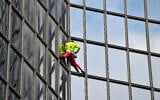 L'alpiniste français Alain Robert, surnommé le "Spiderman français", escalade la tour Coupole Total (qui abrite le siège de Total Energy) à Puteaux, dans le quartier d'affaires de La Défense, à l'ouest de Paris, le 6 novembre 2023, pour lancer un appel à la paix au Proche-Orient. (Crédit : Miguel MEDINA / AFP)