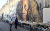 Des hommes passent devant une section de la barrière de sécurité d'Israël peinte d'un portrait de la détenue palestinienne Ahed Tamimi, le 6 novembre 2023 à Bethléem, en Cisjordanie. (Crédit : Hazem Bader / AFP)
